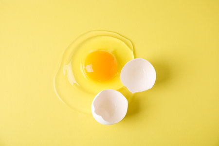 Broken raw egg and shell on yellow background, top viewの写真素材