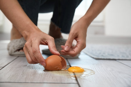 Woman removing shell and broken egg from grey wooden floor indoors, closeupの写真素材
