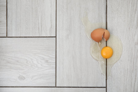 Broken raw egg and shell on light grey wooden floor indoors, top view. Space for text