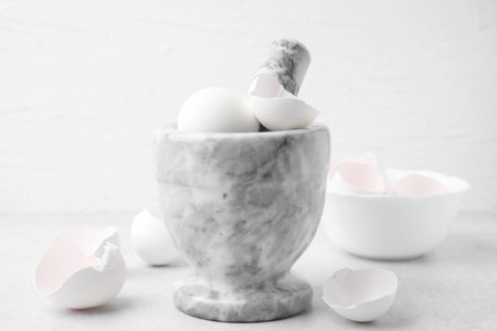 Broken eggshells, mortar and pestle on grey table, closeup