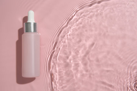 Bottle of cosmetic product in water on pink background, top view. Space for textの写真素材