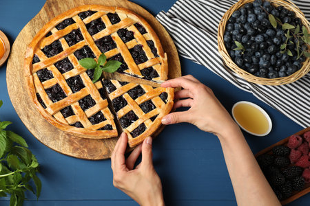 Woman taking piece of tasty homemade pie with blueberries at blue wooden table, top viewの写真素材