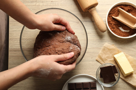 Woman kneading chocolate dough at wooden table, top view