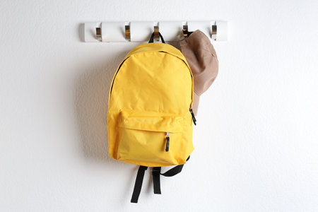 Yellow backpack and cap hanging on white wallの写真素材