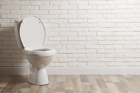 Ceramic toilet bowl near white brick wall in restroom. Space for textの写真素材
