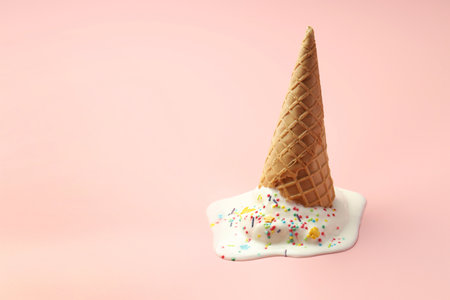 Melted ice cream in wafer cone on light pink background. Space for textの写真素材