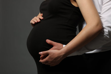 Pregnant woman with her husband touching belly on grey background, closeupの写真素材