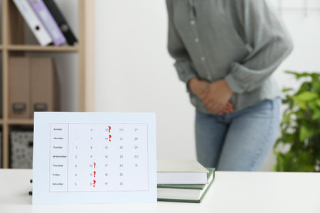 Woman suffering from abdominal pain indoors, focus on calendar with marked menstrual cycle daysの写真素材