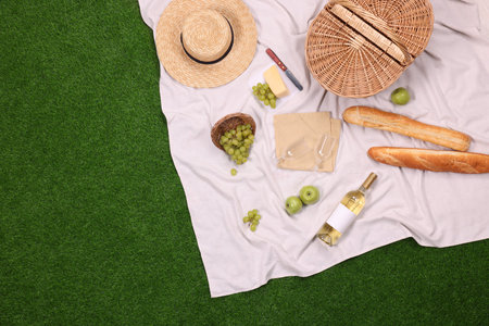 Picnic basket, different snacks, wine and straw hat on green grass outdoors, top view. Space for textの写真素材