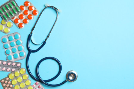 Stethoscope and pills on light blue background, flat lay. Space for textの写真素材