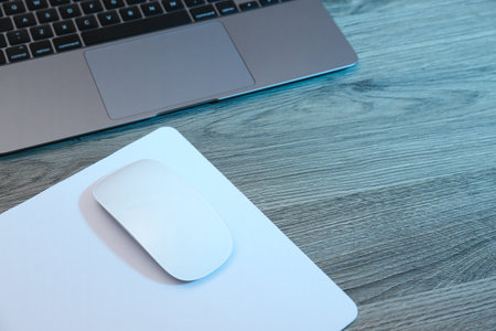 Computer mouse with mousepad and laptop on wooden table. Space for text