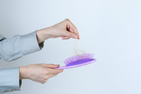 Woman taking lost hair from brush on light grey background, closeup. Space for textの写真素材