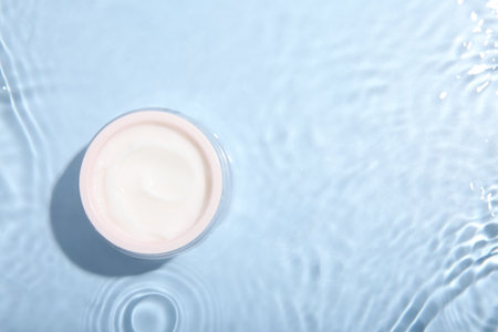 Cosmetic product. Jar with cream in water on light blue background, top view. Space for textの写真素材