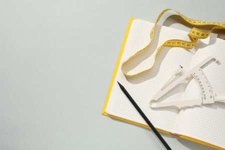 Body fat caliper, measuring tape and notebook on gray background, flat lay. Space for textの写真素材