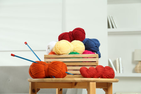 Skeins of soft yarn in crate and knitting needles on wooden table indoorsの写真素材