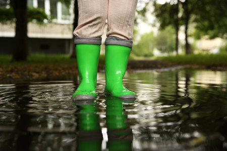 Little girl wearing green rubber boots standing in puddle outdoors, closeup