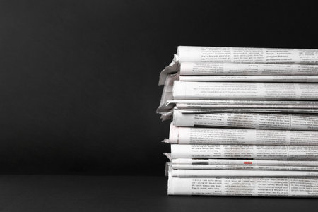 Stack of newspapers in different languages on black background. Space for textの写真素材