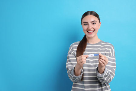 Happy woman holding pregnancy test on light blue background, space for textの写真素材