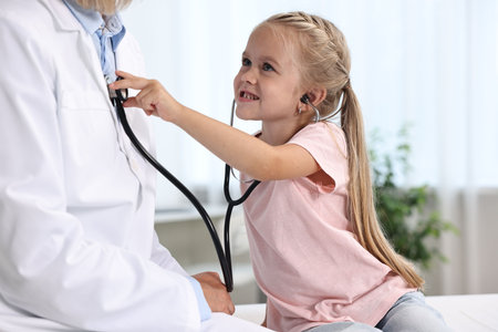Little girl with stethoscope and doctor having fun in hospitalの写真素材