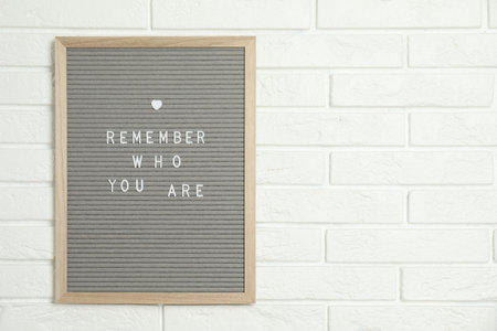 Letter board with phrase Remember Who You Are on white brick wall, space for text