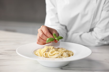 Professional chef decorating delicious pasta with basil at white marble table in kitchenの写真素材