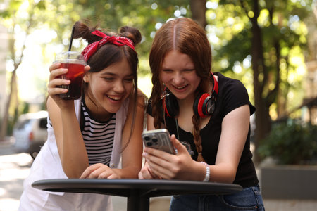 Happy teenage friends looking at smartphone in outdoor cafeの写真素材