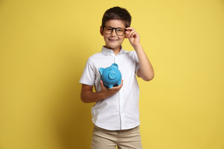 Pocket money. Cute boy with piggy bank on yellow backgroundの写真素材
