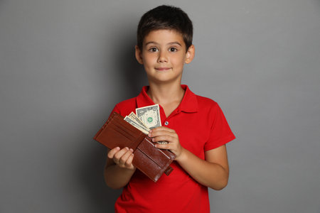 Cute boy with wallet and pocket money on grey backgroundの写真素材