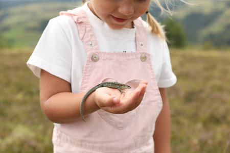 Little girl holding lizard on blurred background, closeup. Child enjoying beautiful natureの写真素材