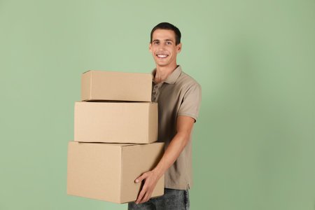 Moving into new house. Man with cardboard boxes on light green background, space for textの写真素材