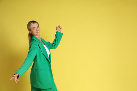 Beautiful woman in stylish green suit posing on yellow background, space for textの写真素材