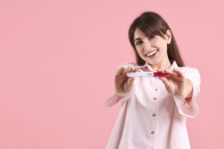 Happy young woman with pregnancy test on pink background, space for textの写真素材