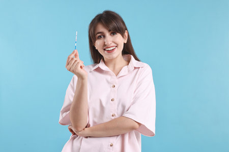 Happy young woman with pregnancy test on light blue backgroundの写真素材