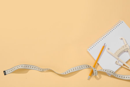 Body fat caliper, measuring tape, pencil and notebook on beige background, flat lay. Space for textの写真素材