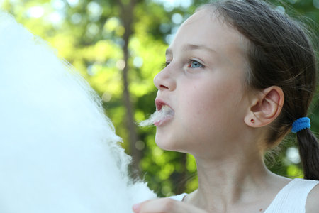 Little girl eating sweet cotton candy in park, closeupの写真素材
