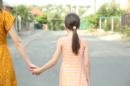 Little girl holding hands with mother outdoors, back viewの写真素材
