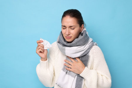 Sick woman with tissue on light blue background. Cold symptomsの写真素材