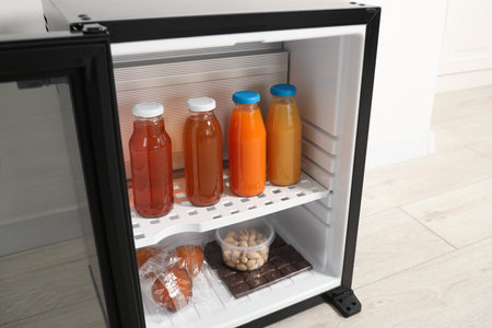 Mini refrigerator with different drinks and snacks near white wallの写真素材