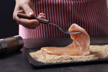 Making schnitzel. Woman slice of meat with bread crumbs at dark table, closeupの写真素材