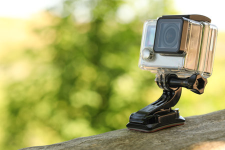 Modern action camera with mount on wooden surface outdoors, closeup. Space for textの写真素材