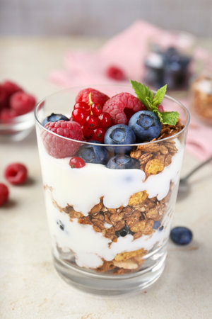 Tasty yogurt with fresh berries, granola and mint in glass on gray textured table, closeupの写真素材