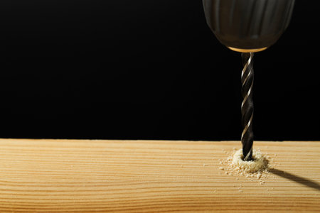 Drilling hole in wooden plank on black background, closeup. Space for text