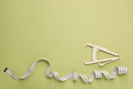 Body fat caliper and measuring tape on light green background, flat lay. Space for text