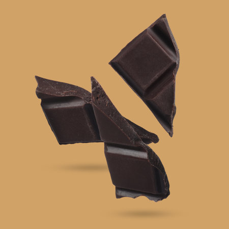 Pieces of sweet chocolate falling on color backgroundの写真素材