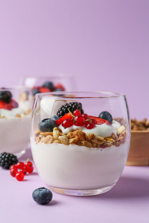 Tasty yogurt with fresh berries and granola in glass on violet backgroundの写真素材