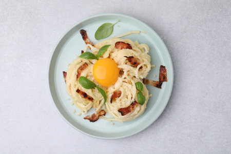 Delicious pasta Carbonara with egg yolk, bacon and basil on light gray table, top viewの写真素材