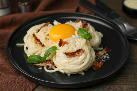 Delicious pasta Carbonara with egg yolk, bacon and basil on wooden table, closeupの写真素材
