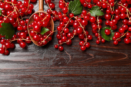 Fresh red currants and green leaves on wooden table, top view. Space for text