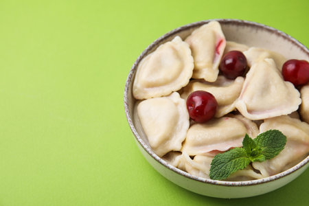 Traditional Ukrainian dumplings (varenyky) with cherries on green background, closeup. Space for textの写真素材