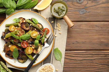 Delicious salad with grilled vegetables, basil, pesto sauce, pine nuts and fork on wooden table, flat lay. Space for textの写真素材